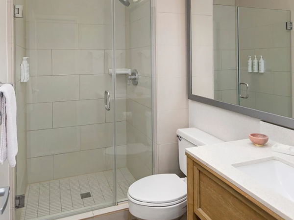 A modern bathroom with a glass-enclosed shower, a wall-mounted toilet, and a wooden vanity with a sink and large mirror, all in neutral tones.