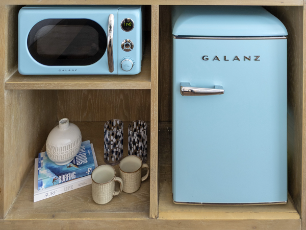 A vintage blue mini-fridge and toaster microwave sit in wooden shelves, with books, mugs, and poker chips nearby.