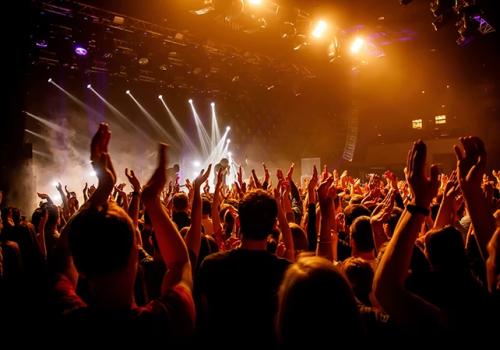 A crowded concert crowd with hands raised, stage lights and performers energizing a lively audience at a music show.
