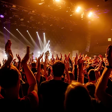 A crowded concert crowd with hands raised, stage lights and performers energizing a lively audience at a music show.