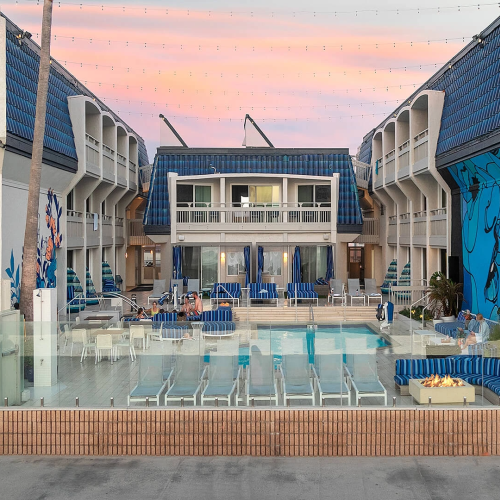 A row of modern buildings with balconies and pastel colors, a courtyard between, under a clear blue sky.