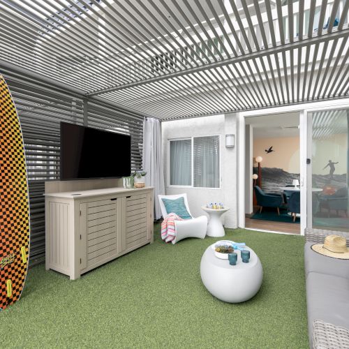 A bright, airy room with a white ceiling, pastel walls, and large windows; clothes hanging on racks, a bicycle, and boxed storage in the corner.