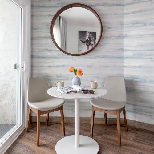 A small round mirror above a white pedestal table with a vase and candles, set in a bright, minimalist entryway with wooden floor.