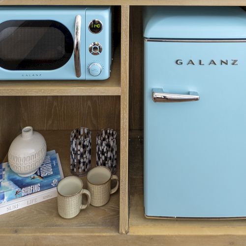 A small blue mini fridge sits next to a wooden box containing a bottle and a pair of shoes, topped by a blue speaker.