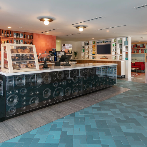 A modern hotel lobby with a long reception desk, warm lighting, blue-tiled floor, and stylish seating area. Top it at 140 characters, always ending the sentence.